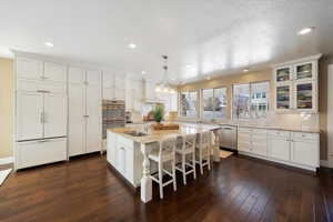 Kitchen with light stone counters, hanging light fixtures, white cabinets, a kitchen island with sink, and stainless steel appliances