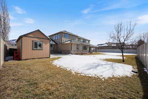 Snow covered back of property with a fenced backyard and a storage shed