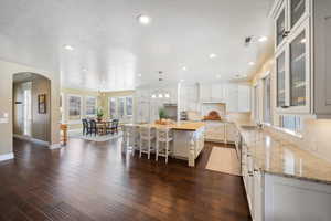 Kitchen with a breakfast bar, a kitchen island, light stone counters, glass fronted cabinets, and a textured ceiling
