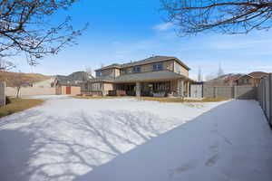 Snow covered property with a storage shed, stone siding, a fenced backyard, and a patio area