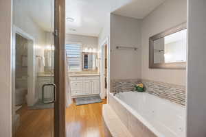 Bathroom featuring vanity, a tub with jets, light wood-style flooring, a shower stall, and a textured ceiling