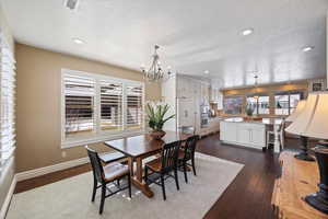 Dining area with dark wood-style flooring, a chandelier, a textured ceiling, and healthy amount of natural light