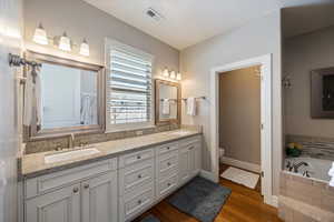 Full bathroom featuring double vanity, a garden tub, and dark wood-style flooring