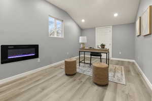 Office with light wood finished floors, recessed lighting, a glass covered fireplace, and vaulted ceiling