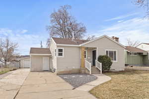 View of front facade featuring a shingled roof, an outbuilding, a front lawn, concrete driveway, and a chimney