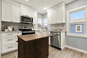 Two tone kitchen with wood counters, stainless steel appliances, light wood-type flooring, tasteful backsplash, and two tone cabinetry