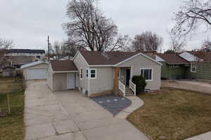 View of front of property with a front yard, an outbuilding, a garage, and a shingled roof