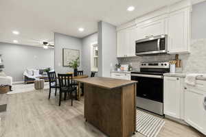Dual tone kitchen featuring stainless steel appliances, butcher block countertops, light wood-type flooring, tasteful backsplash, and a ceiling fan