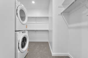 Laundry room featuring light colored carpet, stacked washer and clothes dryer, and recessed lighting