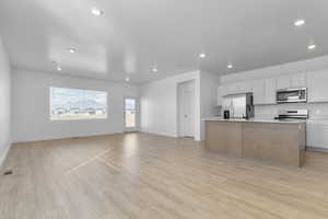 Two tone kitchen with open floor plan, light countertops, a center island with sink, stainless steel appliances, and light wood-style floors