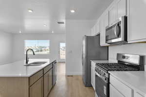 Kitchen featuring stainless steel appliances, light stone countertops, an island with sink, light wood-style flooring, and recessed lighting