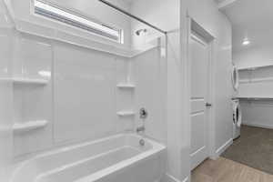 Bathroom with a spacious closet, light wood-type flooring, stacked washing machine and dryer, and washtub / shower combination