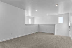Carpeted empty room featuring a textured ceiling and baseboards