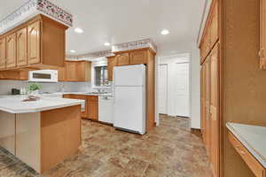 Kitchen with light countertops, white appliances, stone finish flooring, a peninsula, and recessed lighting