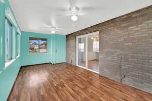 Unfurnished room featuring dark wood-type flooring, brick wall, and ceiling fan