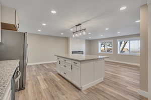 Kitchen with white cabinetry, pendant lighting, light wood-type flooring, and light stone counters