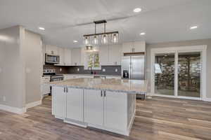 Kitchen featuring light stone countertops, hanging light fixtures, white cabinets, stainless steel appliances, and a kitchen island