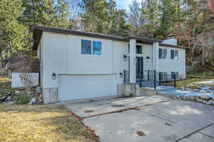 Bi-level home featuring brick siding, a garage, a chimney, and concrete driveway