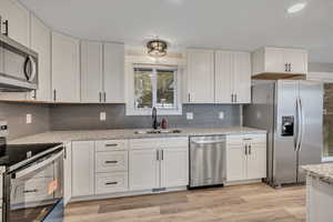 Kitchen featuring stainless steel appliances, white cabinetry, light wood finished floors, light stone counters, and recessed lighting