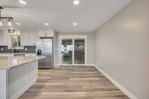 Kitchen featuring stainless steel fridge with ice dispenser, light wood finished floors, white cabinetry, and light stone countertops