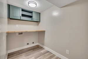 Laundry room featuring a textured ceiling, light wood-style flooring, cabinet space, hookup for a washing machine, and electric dryer hookup