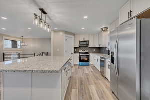 Kitchen featuring stainless steel appliances, a center island, light stone counters, light wood-style flooring, and white cabinetry