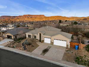 Ranch-style house featuring a garage, a residential view, concrete driveway, stone siding, and a mountain view