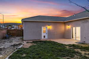 Back of property at dusk with stucco siding and a tiled roof