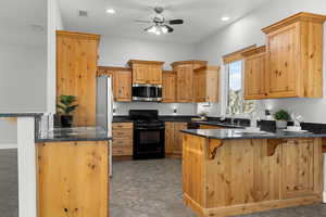 Kitchen featuring a breakfast bar, a peninsula, stainless steel appliances, dark stone counters, and ceiling fan
