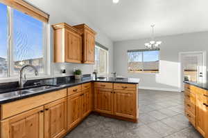 Kitchen with dark stone counters, a chandelier, wood finish cabinetry, and dark tile patterned floors