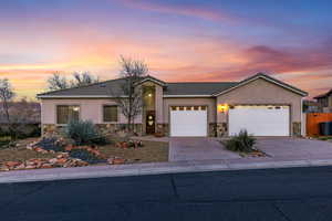 Single story home with stone siding, an attached garage, driveway, stucco siding, and a tiled roof