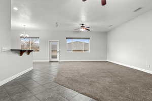 Unfurnished living room with ceiling fan, hanging lights, dark carpet, a textured ceiling, and dark tile patterned flooring