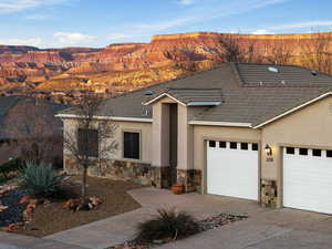 View of front facade featuring an attached garage, stone siding, driveway, stucco siding, and a tiled roof