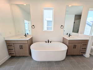 Primary Bathroom featuring two vanities, a freestanding bath, and plenty of natural light