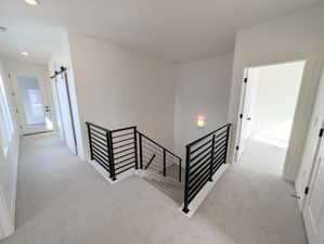 Hallway featuring an upstairs landing, light colored carpet, and a barn door