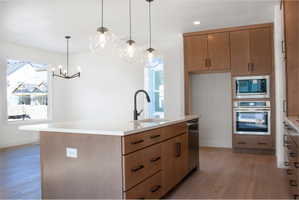 Kitchen with stainless steel appliances, a kitchen island with sink, light wood-style floors, wood finish cabinets, and decorative light fixtures