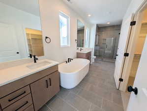 Primary Bathroom with a walk in closet, two vanities, a stall shower, a freestanding bath, and dark tile patterned flooring
