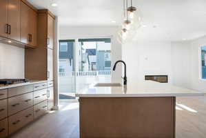 Kitchen featuring a kitchen island with sink, light wood-type flooring, wood finish cabinets, a glass covered fireplace, and hanging light fixtures