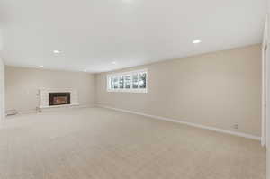Unfurnished living room featuring light colored carpet, a stone fireplace, and recessed lighting