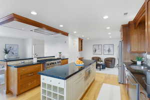 Two tone kitchen with dark stone counters, glass insert cabinets, light wood finished floors, a kitchen island, and stainless steel appliances