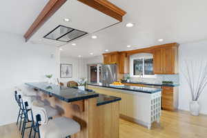 Kitchen featuring a breakfast bar, light wood finished floors, a peninsula, dark stone countertops, and wood finish cabinets