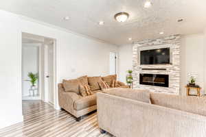 Living room featuring crown molding, a large fireplace, wood finished floors, and a textured ceiling