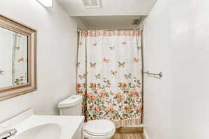 Full bath with a textured wall, vanity, a textured ceiling, curtained shower, and wood finished floors