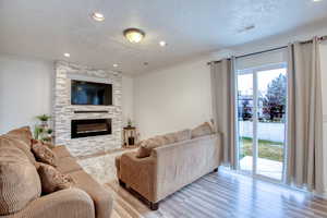 Living area with crown molding, a large fireplace, wood finished floors, a textured ceiling, and recessed lighting