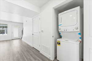 Laundry area featuring stacked washer / drying machine and light wood-style floors