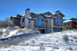 View of front of house with stone siding, an attached garage, and a chimney