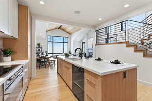 Kitchen featuring modern cabinets, light wood-style floors, an island with sink, stainless steel electric range, and beamed ceiling