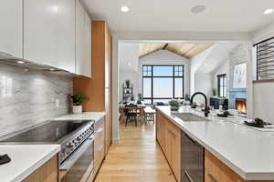 Kitchen featuring stainless steel range, modern cabinets, a lit fireplace, light wood-style flooring, and black dishwasher