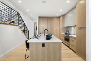 Kitchen featuring modern cabinets, light wood-type flooring, an island with sink, stainless steel electric stove, and a breakfast bar area