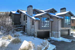 View of front of home featuring a chimney, stone siding, an attached garage, and driveway